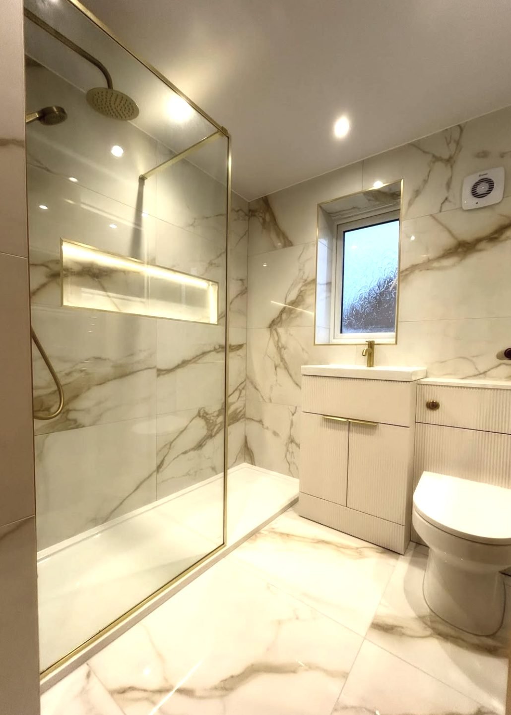 Marble effect bathroom with brushed brass walk-in shower screen and a lit recessed niche